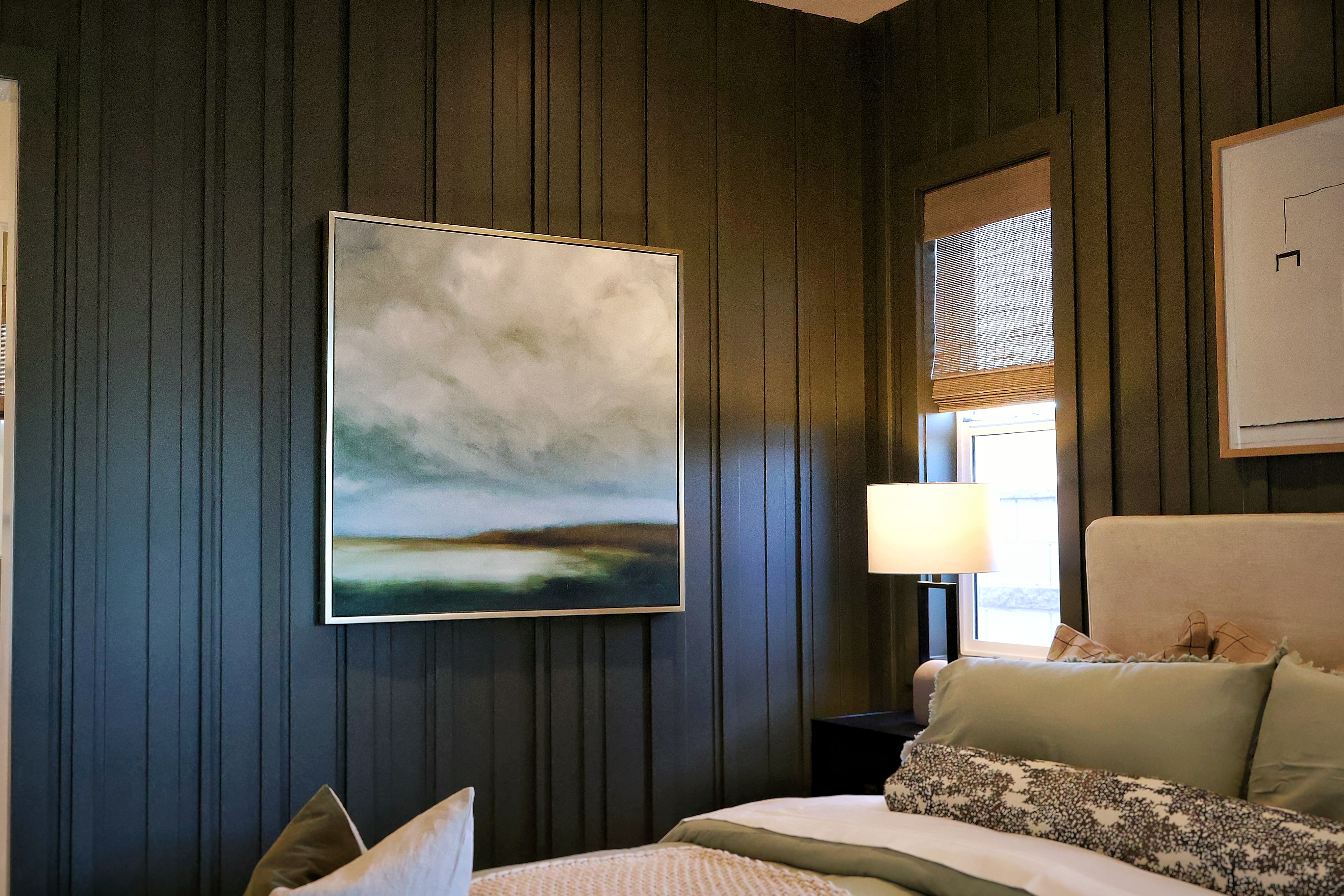 Bedroom with dark olive board and batten accent wall and framed landscape artwork